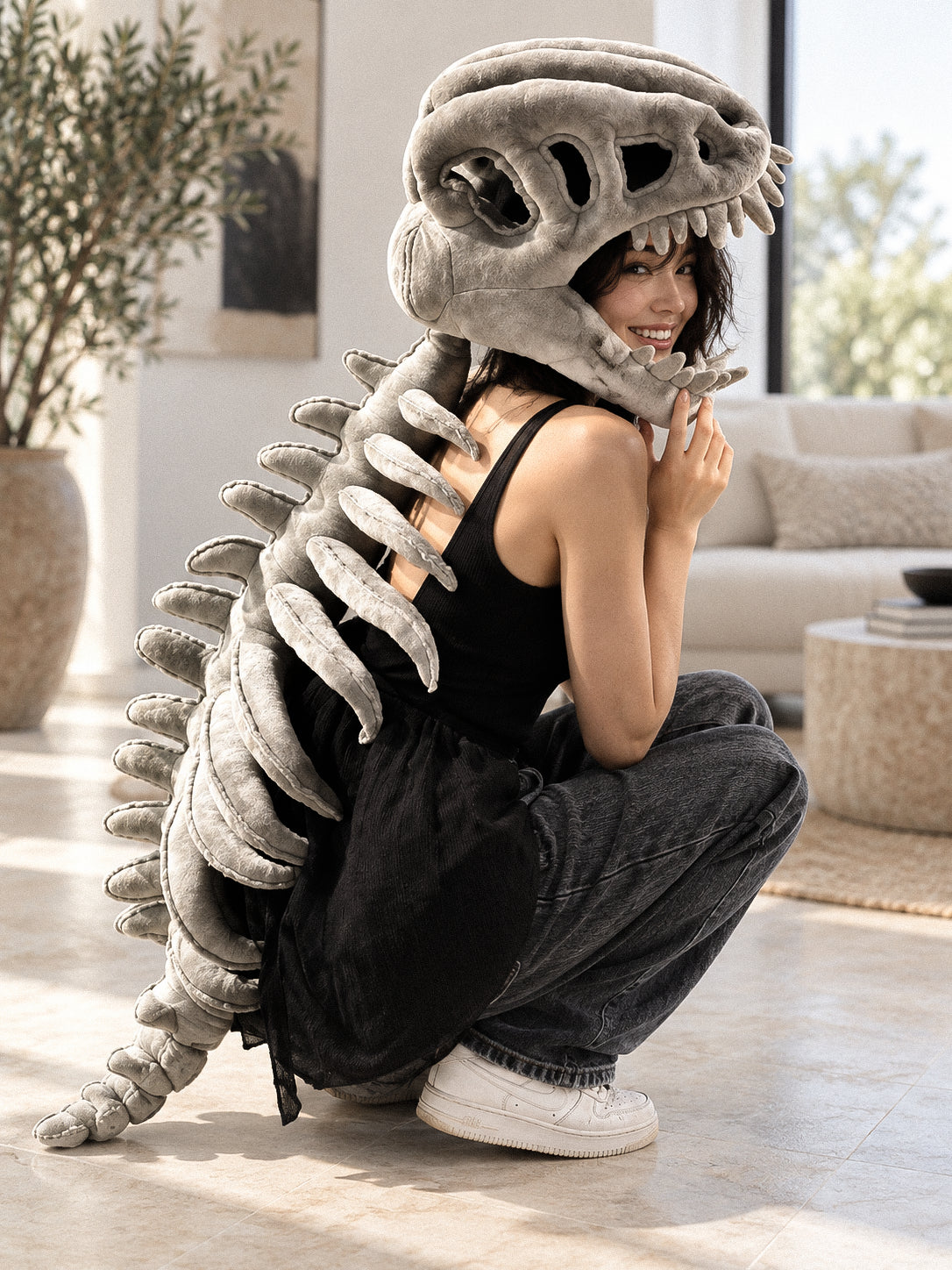Person crouching in a gray plush dinosaur skull hood with sculpted ribs down the back
